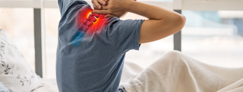 hombre levantándose de la cama con dolor cervical, y esa zona de la espalda marcada en rojo como símbolo de dolor.