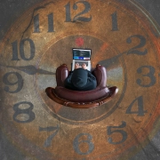 imagen aerea de una mujer sentada con un ordenador en la falda, encima de un reloj grande impreso en el suelo.