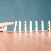 imagen de piezas de domino colocadas una tras otra, con un dedo que empuja una de las piezas para provocar efecto domino.