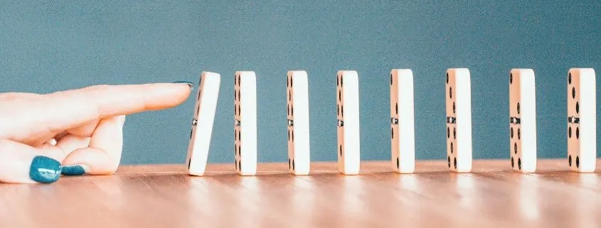 imagen de piezas de domino colocadas una tras otra, con un dedo que empuja una de las piezas para provocar efecto domino.
